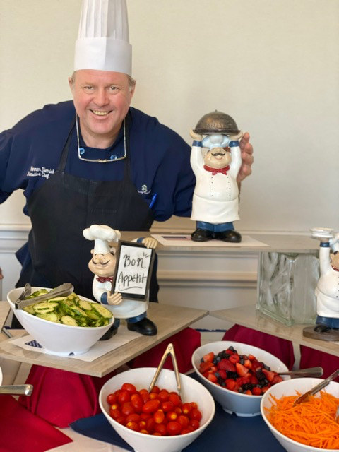 Chef Werner Dietrich in his chef's coat beside a buffet of salads and fresh fruit
